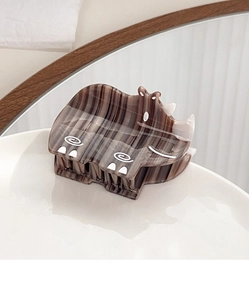 Detail view of a creative rhino-shaped brown acetate hair claw clip on a white ceramic tray