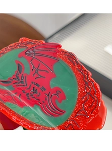 Macro shot of green dragon emblem hair claw with red glitter and wavy acetic acid edge
