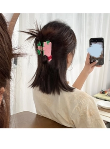 Pince à cheveux fleur rose avec feuilles vertes et nœud rouge portée sur les cheveux