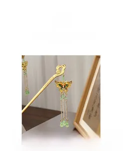 Detail of golden butterfly hair stick with green beads and metallic tassel chains