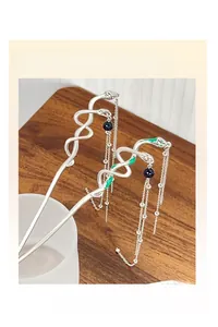 Silver snake-shaped hairpins with long tassels and green crystal accents on a wooden desk