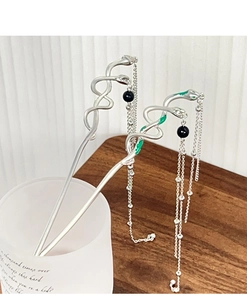 Detail of silver snake hairpins with green enamel and long tassel chains on wood