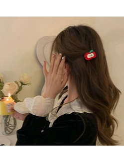 Close-up of red apple acetate hair clip worn on model with warm ambient lighting