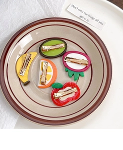 Set of five vibrant acetate fruit hair clips including orange and kiwi on a ceramic plate