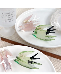 Detail of pink and green swallow-shaped hair claws with marble texture on ceramic plate