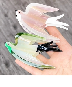 Detail of bird-shaped acetate hair claws in swallow and dove designs held by hand
