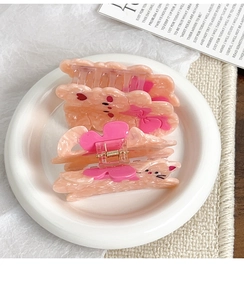 Gros plan de pinces à cheveux en acétate rose avec motifs chat et nœud sur plat blanc