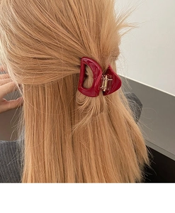 Détail d'une pince à cheveux rouge foncé en forme de D sur de longs cheveux bruns
