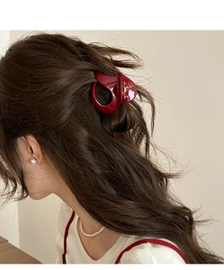 Close-up of a dark red pumpkin hair claw clip securing a ponytail on brown wavy hair