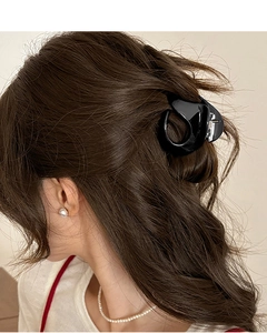 Side view of a glossy black minimalist pumpkin hair claw clip on wavy brown hair