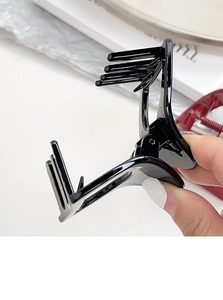 Détail d'une petite pince à cheveux triangulaire noire brillante tenue à la main