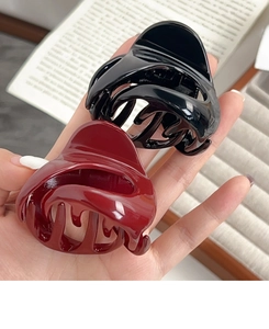 Detail of glossy black and wine red pumpkin hair claws held in hand for hair styling