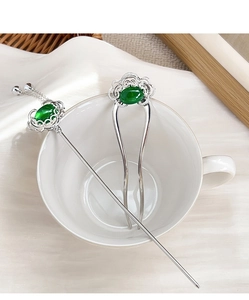 Detailed macro of silver vintage hair pins with green stone and tassel in white ceramic