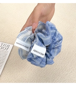 Detail showing blue and white striped fabric scrunchie with woven labels and stitched edges