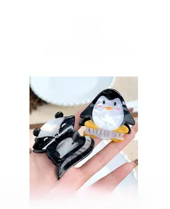 Detail of cute penguin and panda acetate hair claws with marble texture held in hand