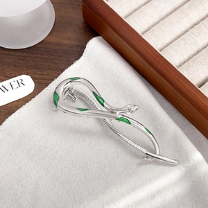 Silver snake hair claw clip with green enamel accents on a textured white fabric base