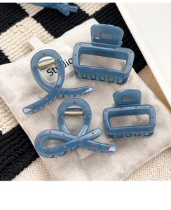 Detail view of blue resin hair claws with red dots on beige fabric background