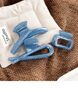 Close-up of three blue polka dot hair claws on textured fabric and a cotton bag