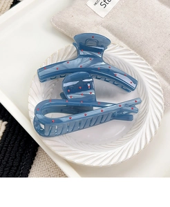 Detailed view of dark blue resin hair claw clips with red polka dots on white tray