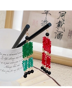 Détail de boucles d'oreilles chinoises Xi à pompons rouges et verts sur des baguettes noires
