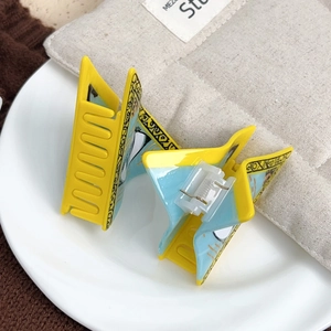 Paire de pinces à cheveux en acétate jaune et bleu avec motifs yeux du diable sur plat blanc