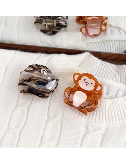 Detailed view of acetate hair claws in animal shapes on a white knit fabric background