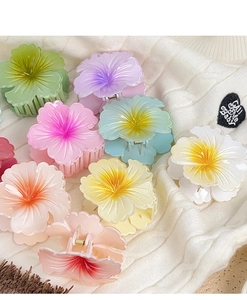 Detailed view of colorful gradient plumeria hair claws on a soft white fabric background