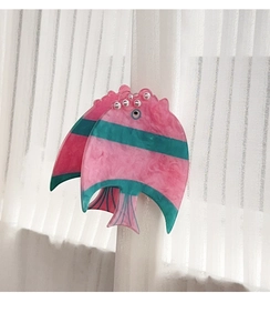 Vue détaillée d'une pince à cheveux poisson en acrylique avec perles sur rideau blanc