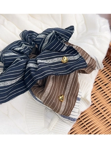 Detail of striped bow scrunchie with a gold heart pendant on a white knit fabric