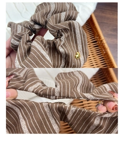 Detail of striped brown scrunchie showing fabric elasticity and golden heart charm