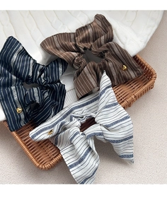 Close-up of striped fabric scrunchies in navy, coffee and cream with gold heart charms