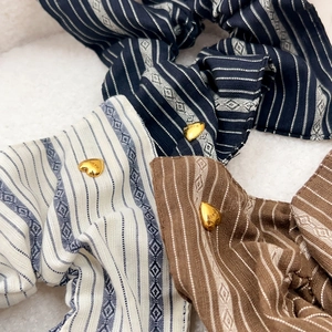Three striped fabric hair scrunchies with golden heart charms in navy, beige, and coffee
