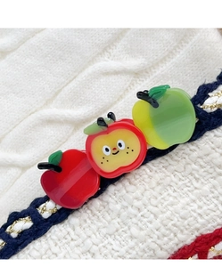 Detailed macro view of cute apple-shaped acetate hair clips on white knit fabric texture