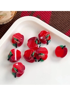 Close-up of small red apple shaped hair claws in a white tray with metal spring detail