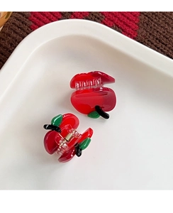 Close-up of two mini red apple hair clips with green leaf detail on a white ceramic plate