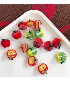 Detail of red apple shaped acetate hair claws with cartoon expressions on a plate