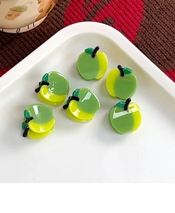 Close-up of cute green and yellow apple-shaped hair clips in a white tray