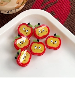 Detail view of small red apple hair clips with cute faces on a white tray