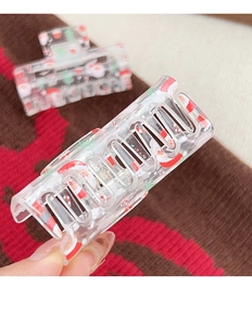 Detail of transparent Christmas claw clip with Santa prints on festive sweater background
