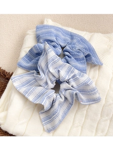 Vue détaillée de chouchous à rayures bleu clair et beige sur fond de pull blanc torsadé