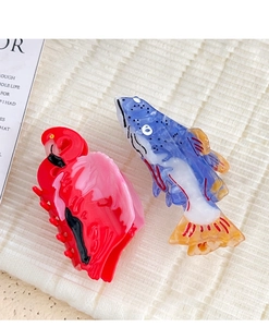 Detailed close-up of colorful acetate flamingo and tropical fish hair claw clips on woven fabric