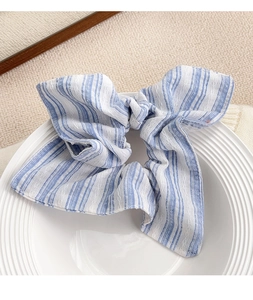 Gros plan d'un chouchou à rayures bleues et blanches avec long nœud sur plat de céramique