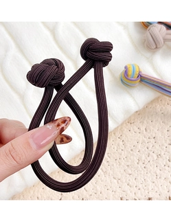 Detail of two dark brown elastic hair ties with button knot design on soft knit background