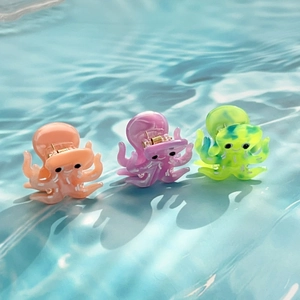 Three octopus-shaped acetate hair clips in pastel marble colors on blue water texture