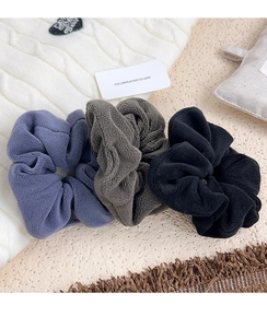 Detail of plush velvet scrunchies in purple, grey, and black on a soft knit background