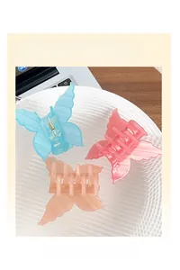 Three acrylic butterfly hair claws in pastel blue, pink, and peach on a textured white plate