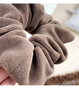 Close-up of soft brown plush scrunchie showing fluffy fabric texture and elastic band