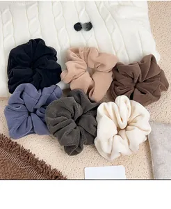 Close-up of six textured plush scrunchies in autumn colors on a white knit sweater