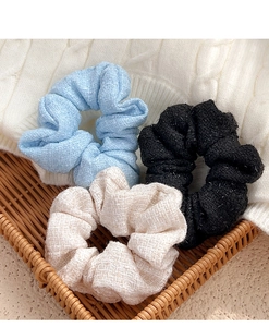 Close-up of tweed scrunchies in blue, beige, and black with silver glitter details