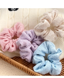 Close-up of four tweed scrunchies in pastel colors on a white knitted sweater